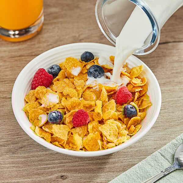 A bowl of Corn Flakes cereal with berries and milk on a table with a spoon and a napkin.