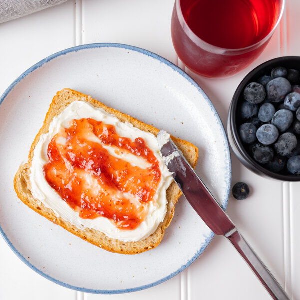 White plate with toast, covered in mascarpone with jam, blueberries, and juice in the background