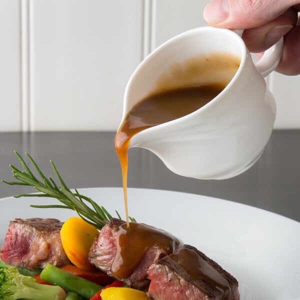 A person pouring LeGout beef gravy on meat and vegetables on a table.