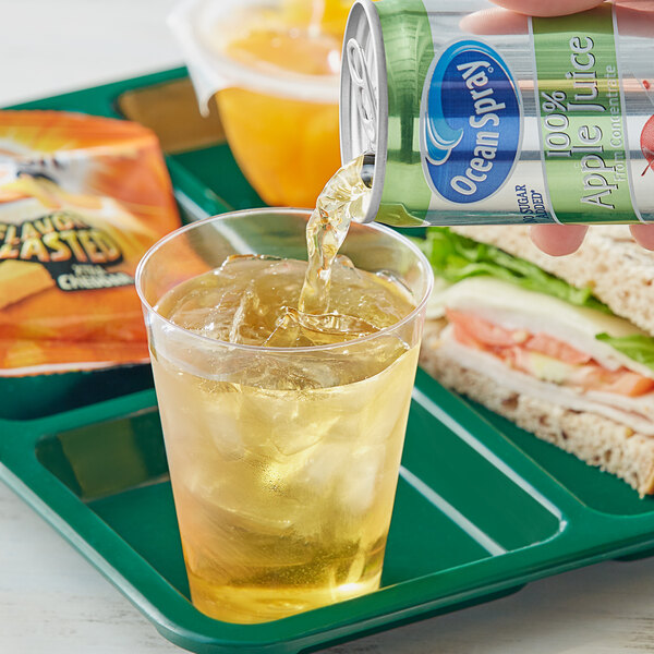 A hand pouring Ocean Spray Apple Juice into a glass of ice.