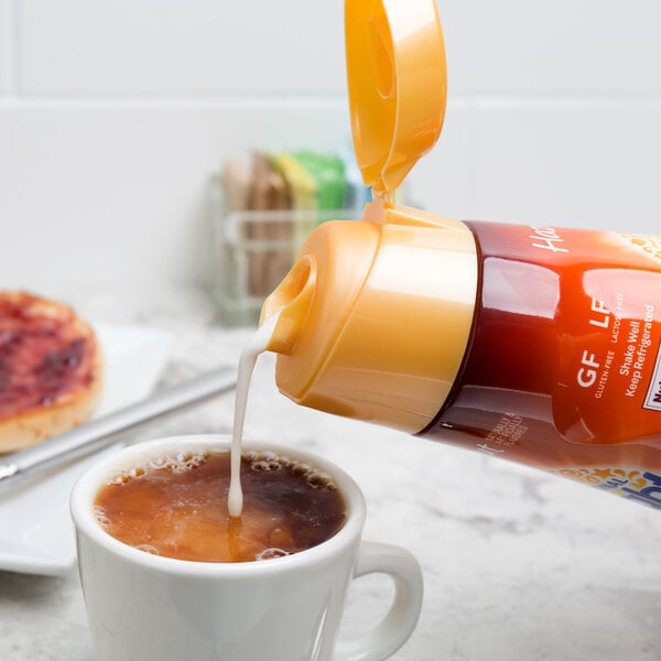 A person pouring International Delight Hazelnut Coffee Creamer into a cup of coffee.