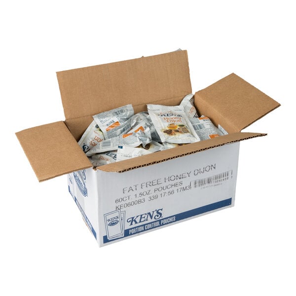An open cardboard box containing multiple individual packets of Ken's fat-free honey dijon dressing.