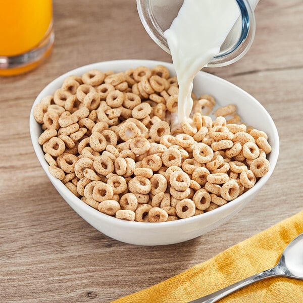 A bowl of Cheerios cereal with milk being poured into it.