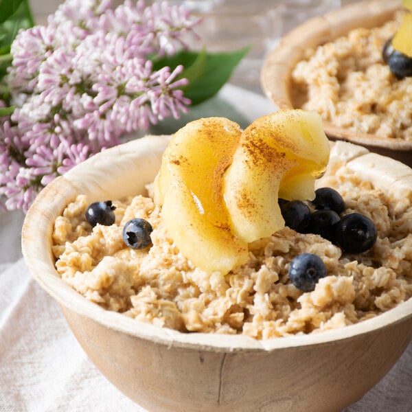 A white bowl of oatmeal topped with frozen green apple slices, blueberries, and fruit.