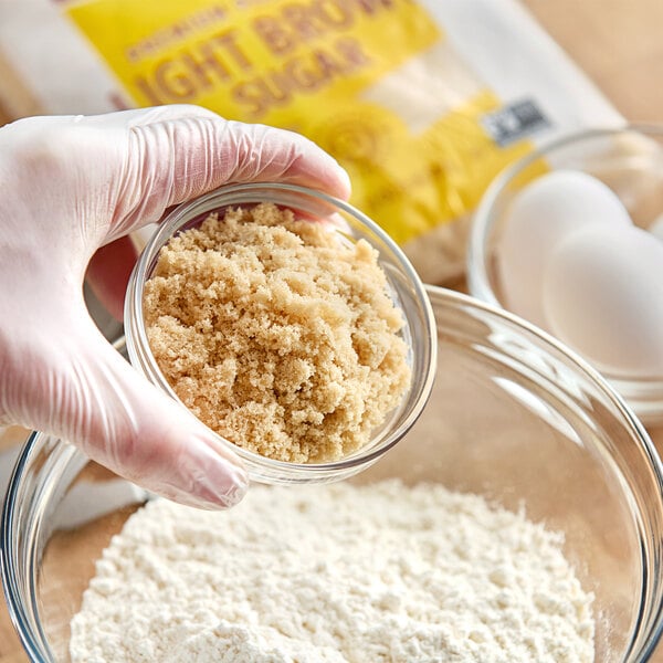 A person holding a bowl of Domino light brown sugar.