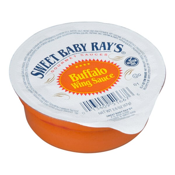 A small, round, single-serve cup with an orange base and a sealed lid labeled 'Sweet Baby Ray's Buffalo Wing Sauce.'