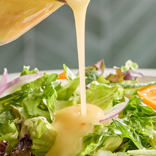 A fresh salad being topped with a creamy Italian dressing.