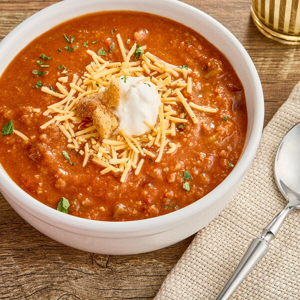 A bowl of Chef Francisco Timberline Chili with cheese and sour cream on a wood surface.