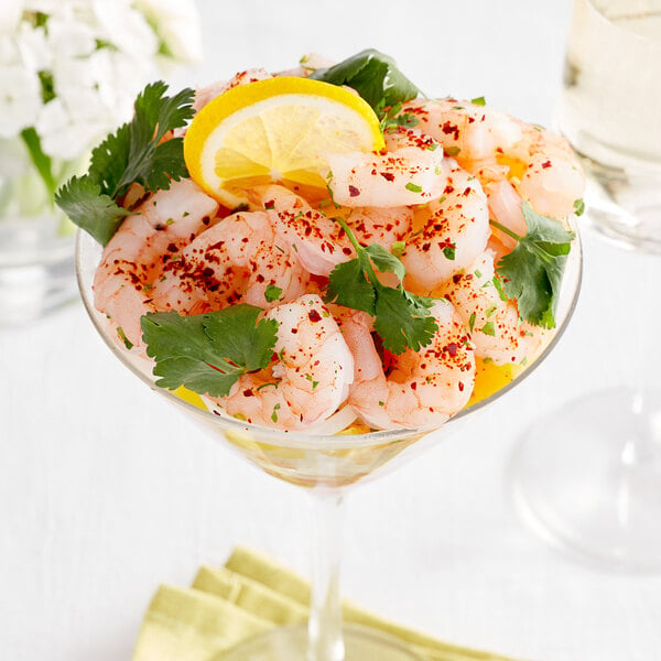 Small sized shrimp in a cocktail glass with cilantro leaves and a slice of lemon