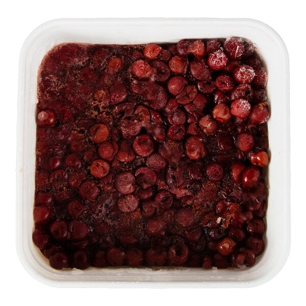 A square plastic container filled with frozen red tart pitted cherries.