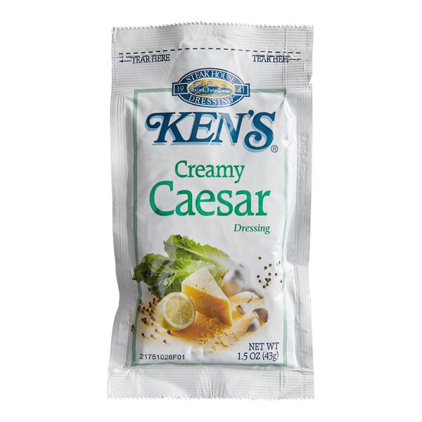 A single-serve packet of Ken's Creamy Caesar Dressing with images of lettuce, cheese, lemon, and peppercorns on the front.