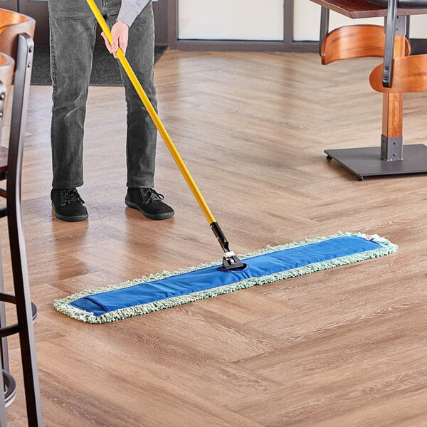 A man using a Lavex all-in-one microfiber dust mop to clean a hardwood floor.