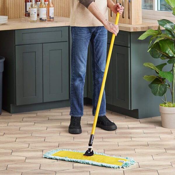 A person using a Lavex all-in-one microfiber dust mop with a long handle to clean the floor.