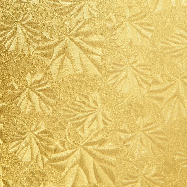 A close up of a gold patterned surface with floral designs on an Enjay gold round cake drum.