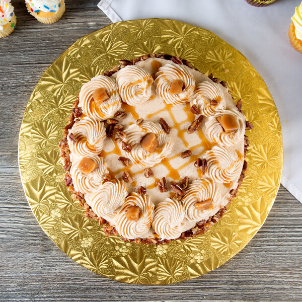 A cake with caramel frosting and pecans on a gold Enjay cake drum.