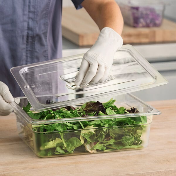 A person in gloves using a Cambro clear plastic lid to cover a container of salad.