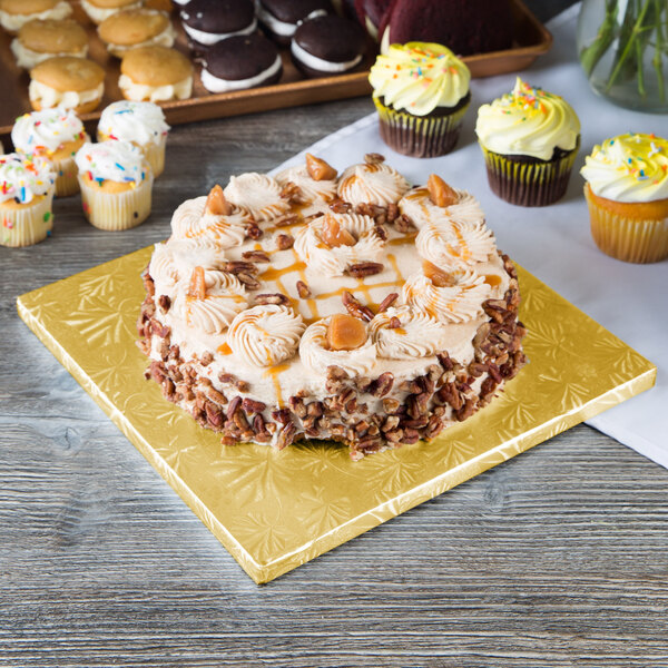 A cake with frosting and pecans on a gold Enjay square cake drum on a table.