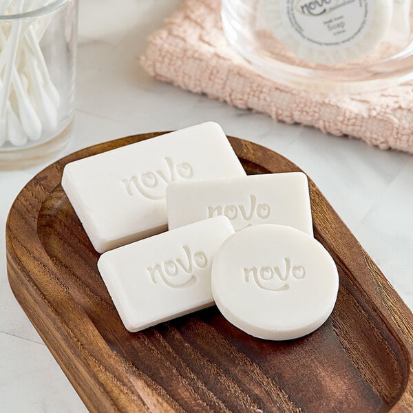 A group of Novo Essentials wrapped round white bath soaps on a wooden tray.