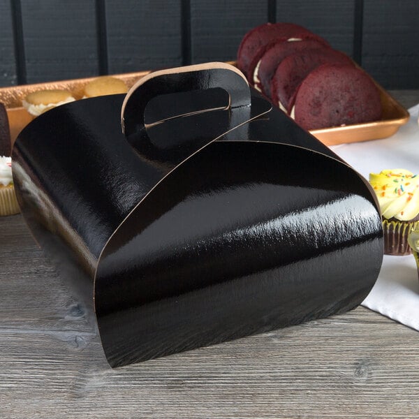 A black Enjay quad cupcake tulip box with a handle next to a tray of cupcakes.