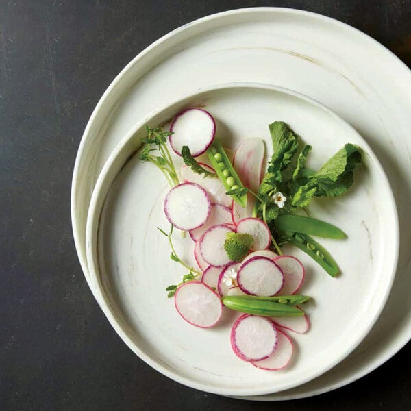 A Oneida Marble porcelain plate with a raised rim holding a plate of vegetables and greens on a table.