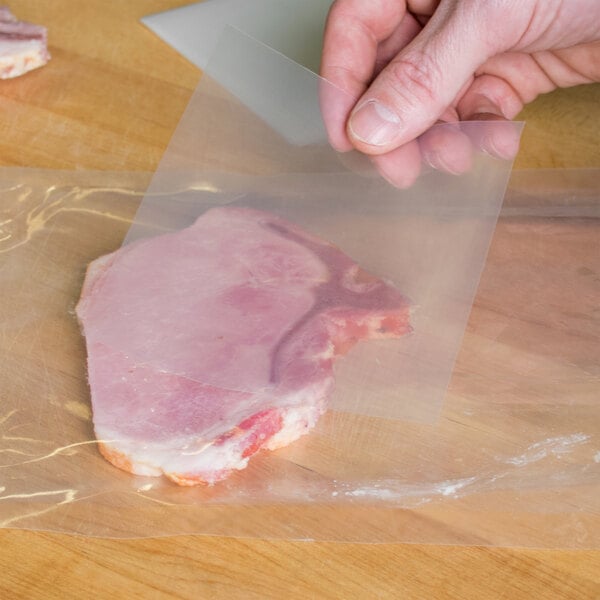 A hand holding a piece of meat being placed in a VacPak-It bone guard bag.