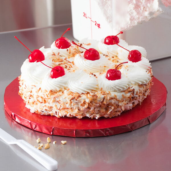 A cake with whipped cream and cherries on a red Enjay round cake drum.