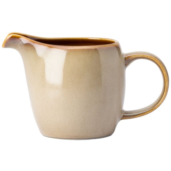 A cream colored ceramic Oneida Rustic Sama creamer with a brown handle.