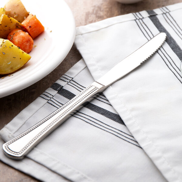 A Oneida Needlepoint stainless steel dinner knife on a plate of food.