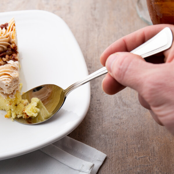 A hand holding a Oneida Needlepoint oval bowl spoon over a piece of cake.