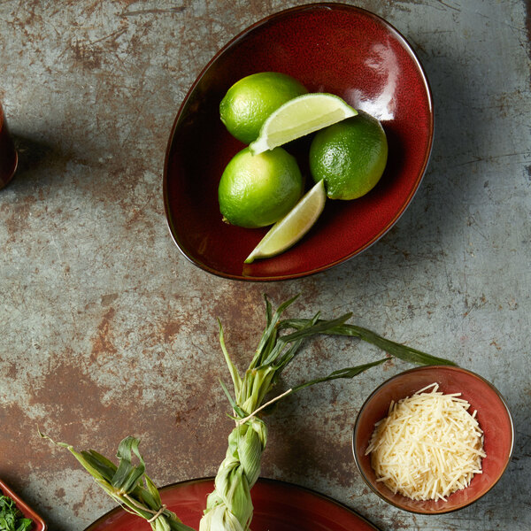 A Oneida Rustic crimson porcelain soup bowl filled with limes and a slice of lime.