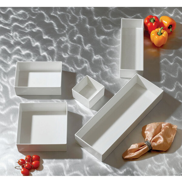 A group of white rectangular Bon Chef bowls filled with vegetables.