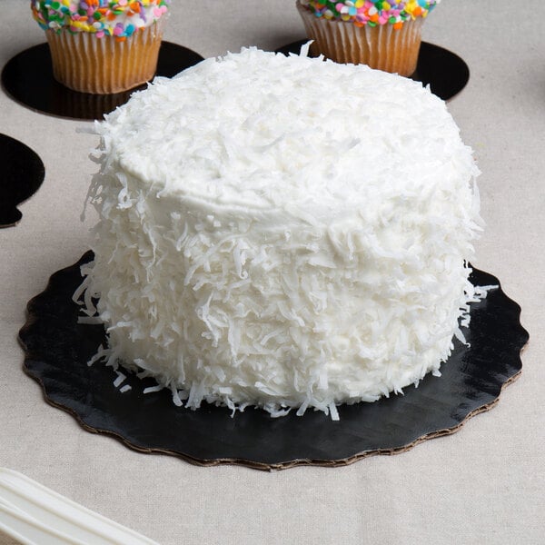 A white cake with white frosting and cupcakes on a black Enjay cake circle.