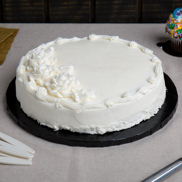 A white cake on an Enjay black round cake drum on a table with a knife and candles.