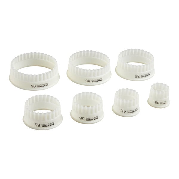 Seven white, round, fluted pastry cutters of varying sizes are arranged in two rows on a white background.