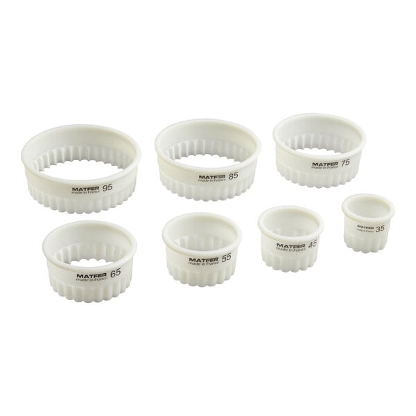 Seven white, round, fluted pastry cutters of varying sizes are arranged in two rows on a white background.