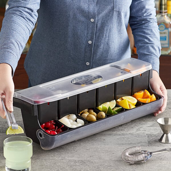 A woman holding a Tablecraft condiment bar with containers of fruit.