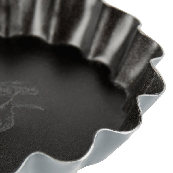 A close up of a black fluted Matfer Bourgeat tartlet/quiche mold.