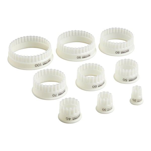 Nine white, round, fluted pastry cutters of varying sizes are arranged in a group on a white background.