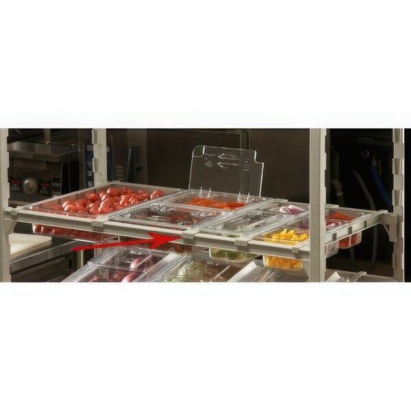 A white Cambro food storage rack with a divider bar on a shelf holding trays of vegetables.