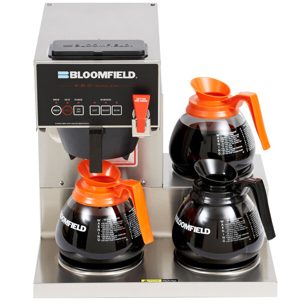 A Bloomfield automatic coffee maker with three orange coffee pots on a counter.