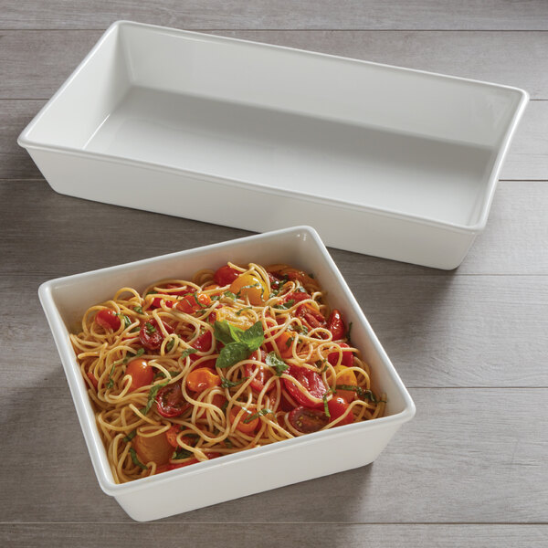 An American Metalcraft white rectangular porcelain bowl filled with pasta and vegetables on a wood surface.