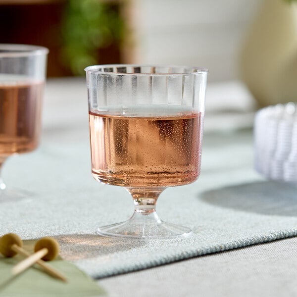 A clear plastic pedestal wine cup filled with a sparkling beverage.