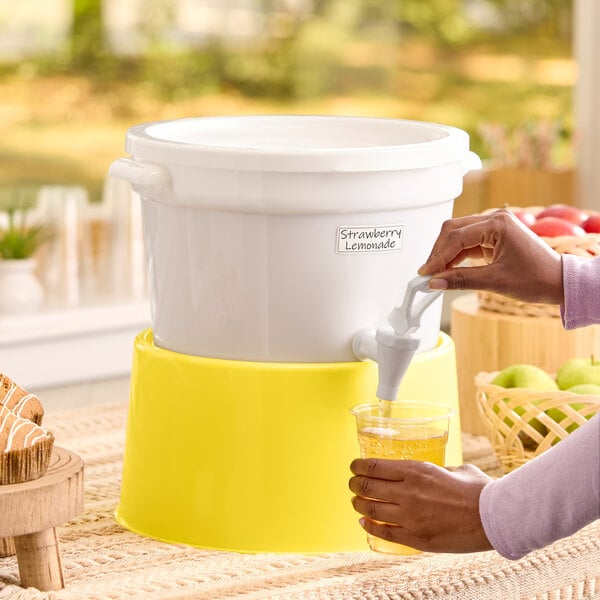 A white round beverage dispenser with a yellow base being used to pour a drink into a cup.