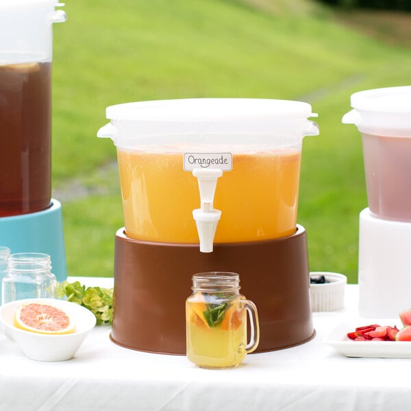 A Choice translucent plastic beverage dispenser with a brown base full of pink liquid on a table.