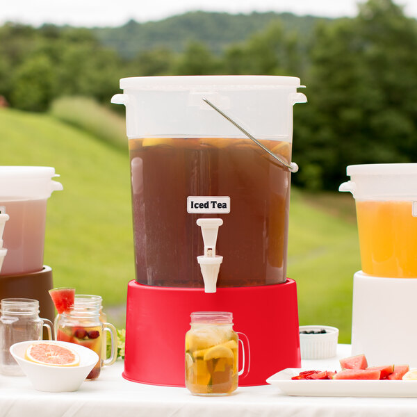 A Choice translucent plastic beverage dispenser with a red base filled with a clear drink and orange slices.