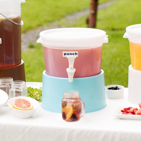 A white Choice beverage dispenser with a blue base on a table outdoors with fruit and juice.