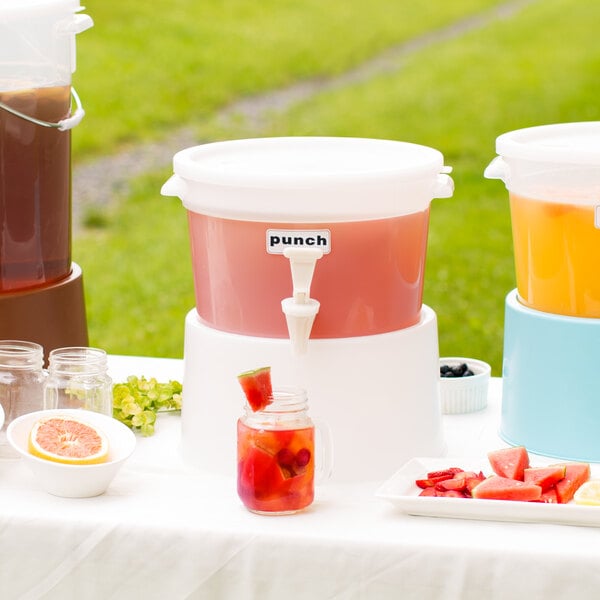 A white table with a Choice white beverage dispenser filled with orange liquid and a jar of fruit on it.