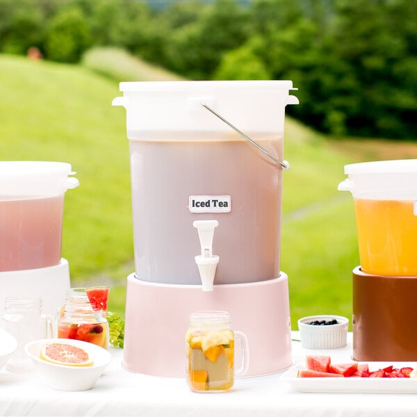 A white Choice beverage dispenser with a pink drink on a table with a glass of fruit.