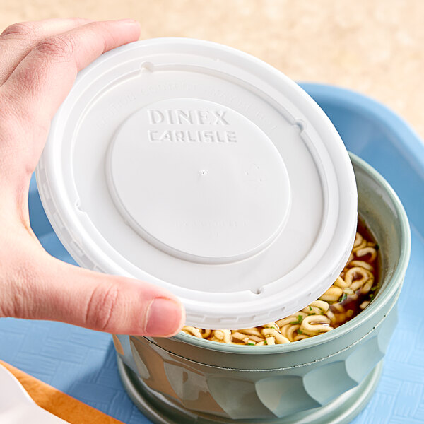 A hand using a Dinex translucent plastic lid to cover a bowl of noodles.