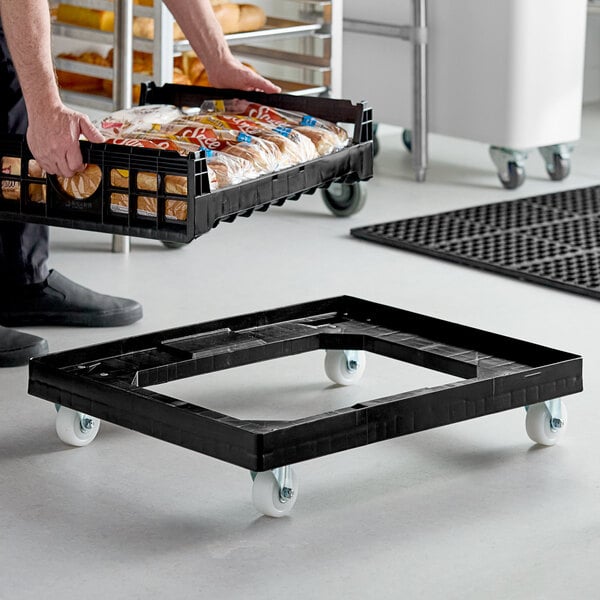 A man using an Orbis Bakery Tray Dolly to transport a black crate full of bread.